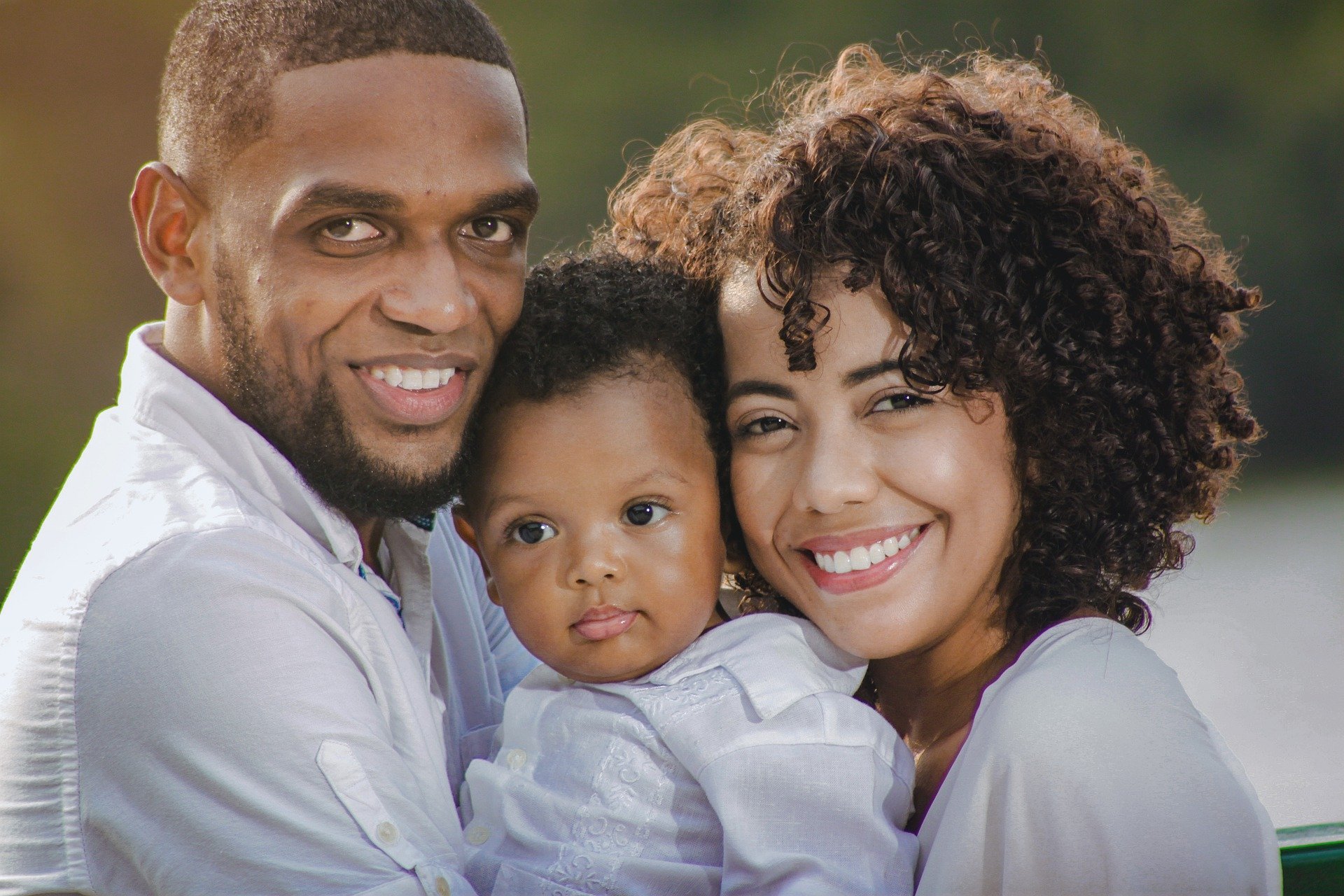 Homem e mulher, ambos negros, sorrindo e segurando bebê
