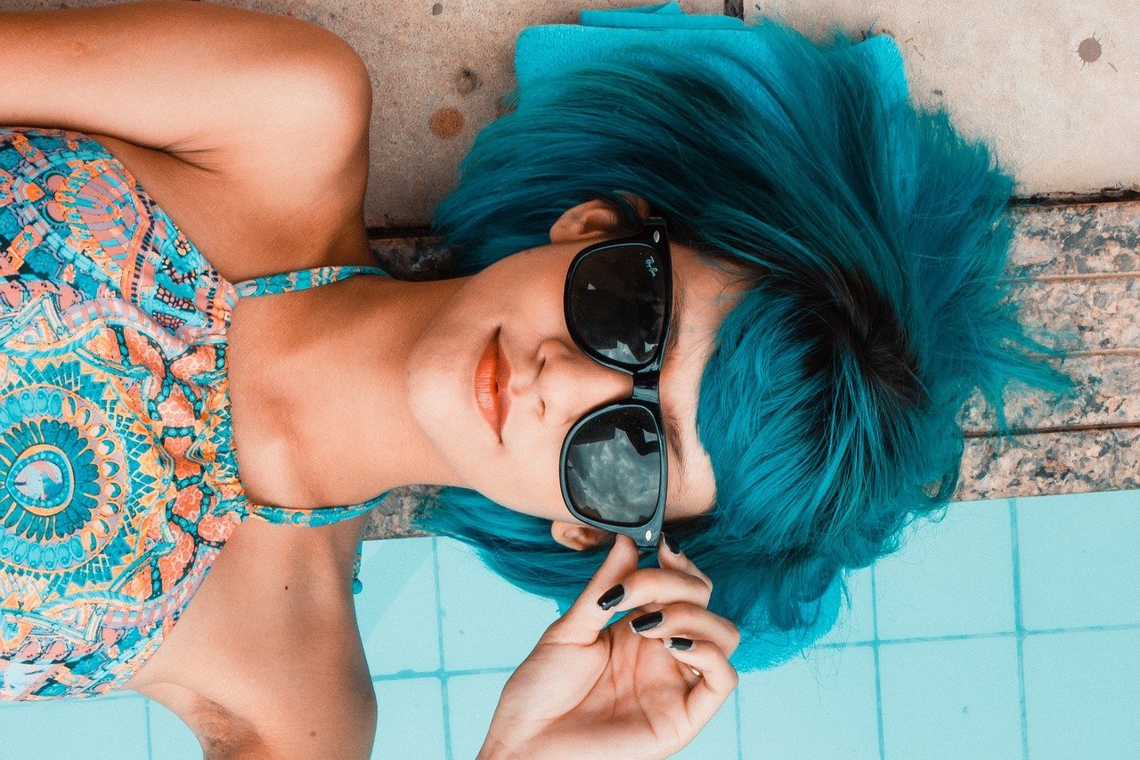 Menina de cabelos azuis deitada em beira de piscina