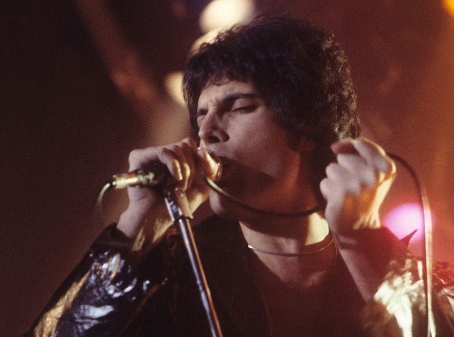 Freddie Mercury segurando o microfone de fio e de olhos fechados cantando