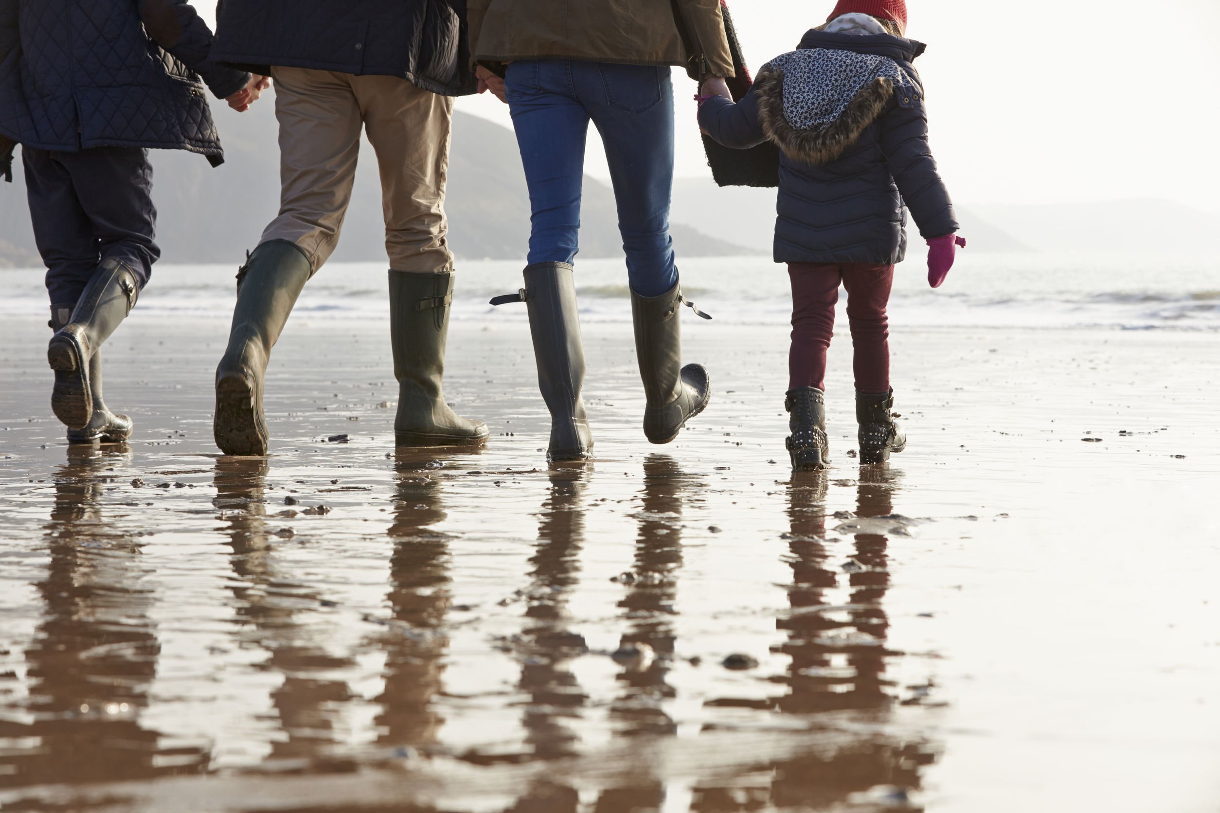 Família caminhando de mãos dadas em praia.