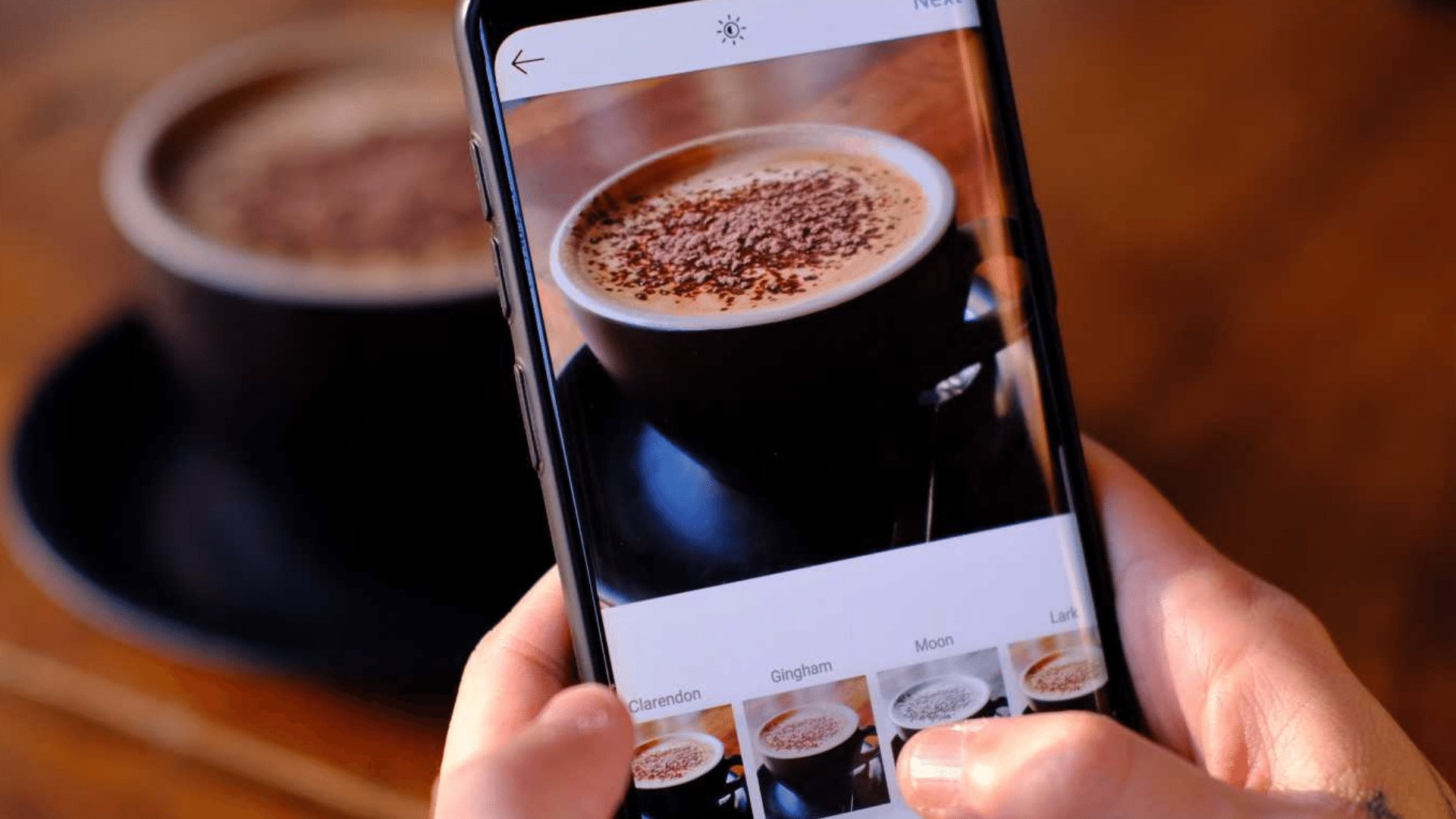 Pessoa editando no instagram uma foto de uma xícara de café que está na sua frente em cima da mesa