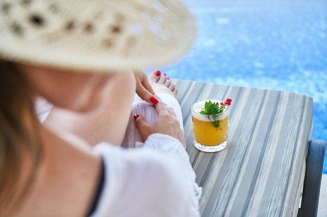Mulher em espreguiçadeira de frente a piscina e drink ao seu lado
