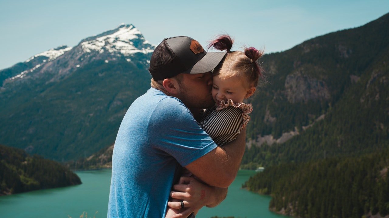 Pai beija filha enquanto a segura nos braços.