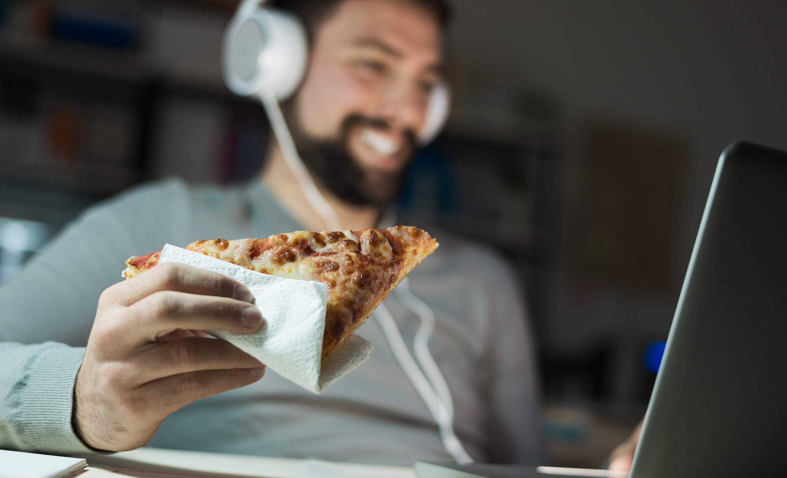 Homem usando computador e comendo pizza