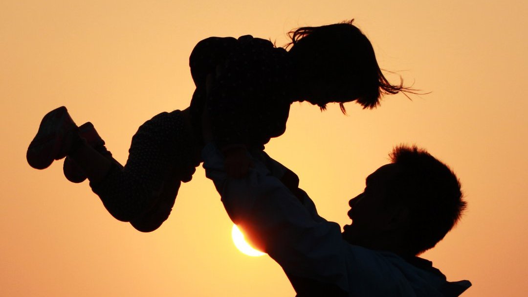 Silhueta de pai erguendo filha durante o por do sol