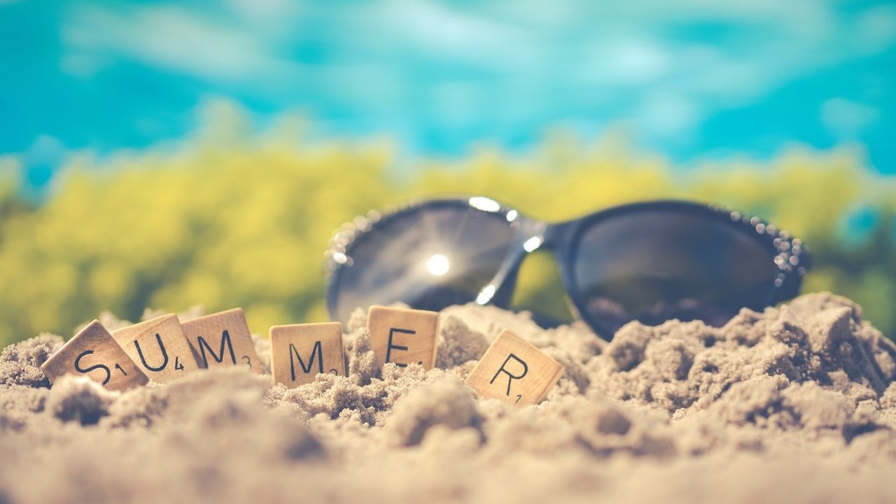 Óculos de sol na areia da praia com pequenos quadrados escritos 'summer', que significa verão.