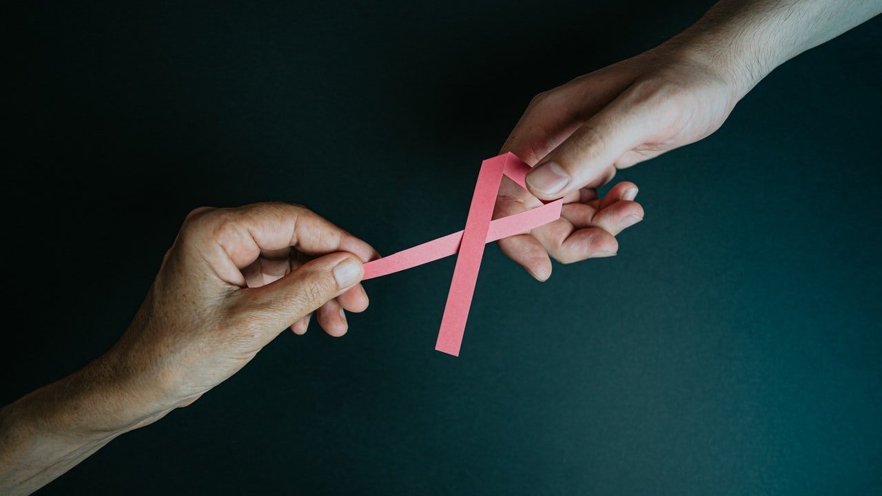 Duas mãos seguram o laço rosa representativo do combate ao câncer de mama.