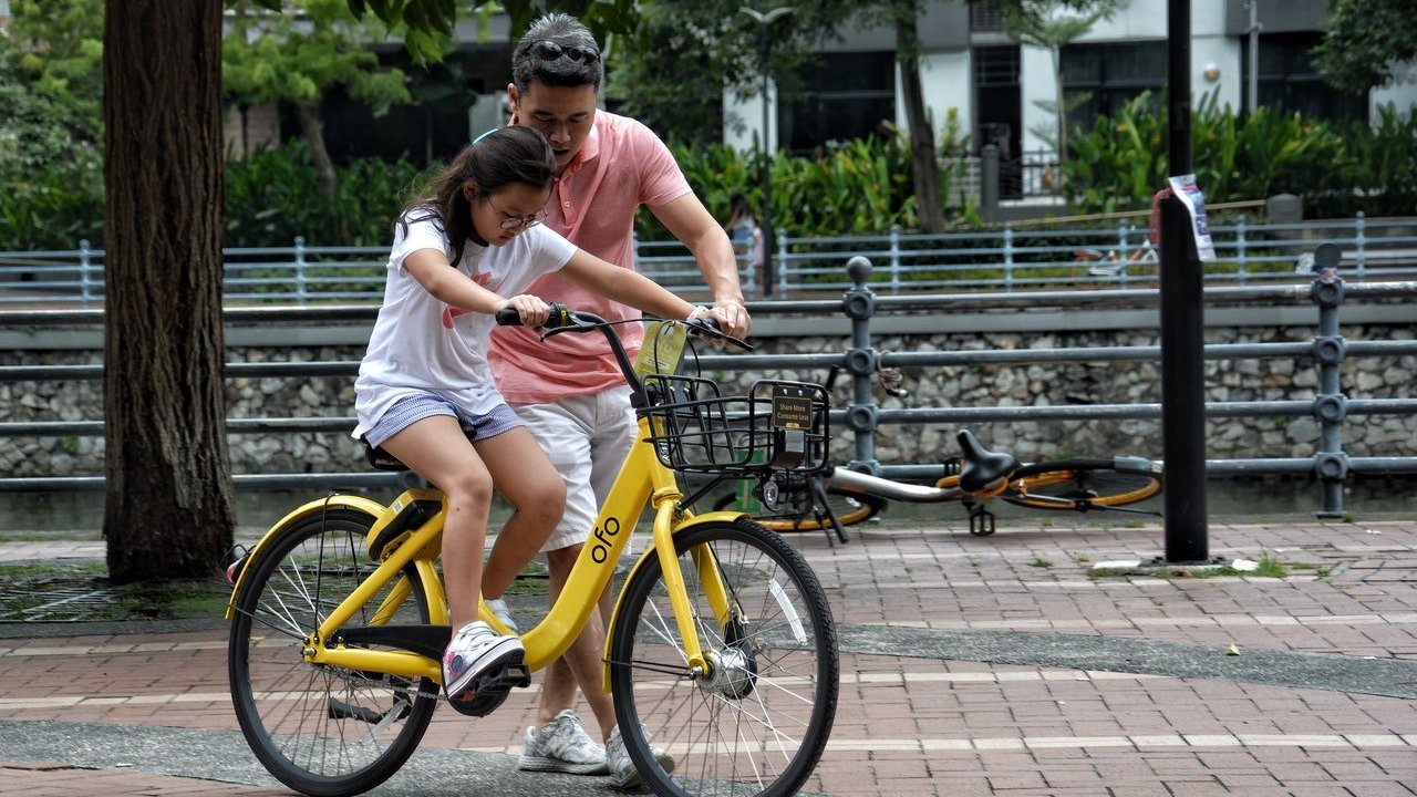 Pai ensina filha a andar de bicicleta.