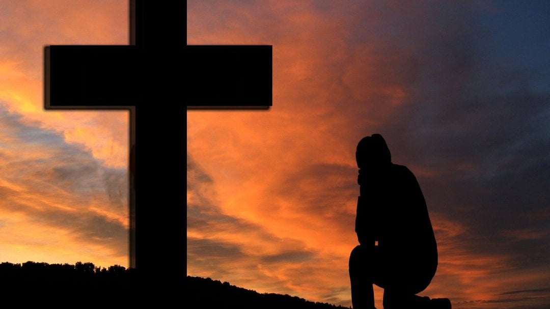 Homem ajoelhado em frente a cruz