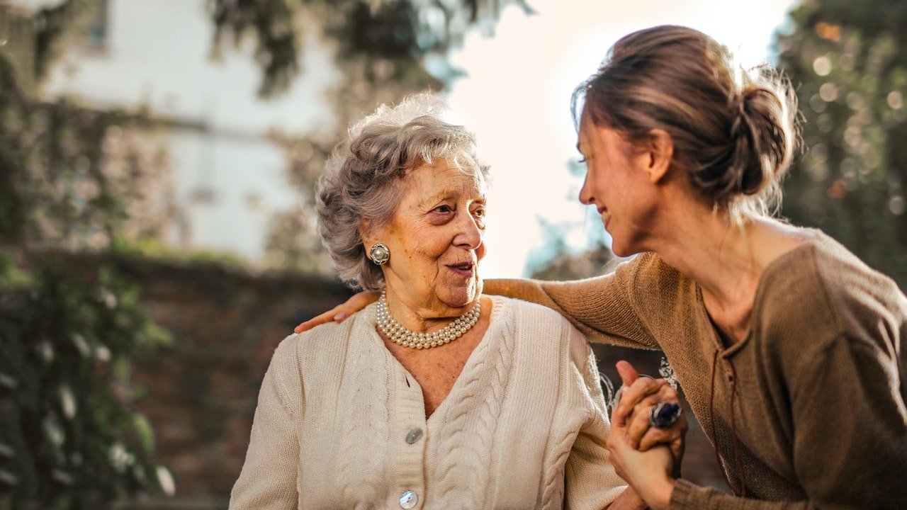 Mulher adulta conversa com idosa.