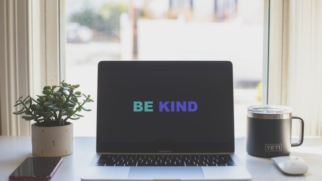 Computador aberto com a frase 'Be kind'.