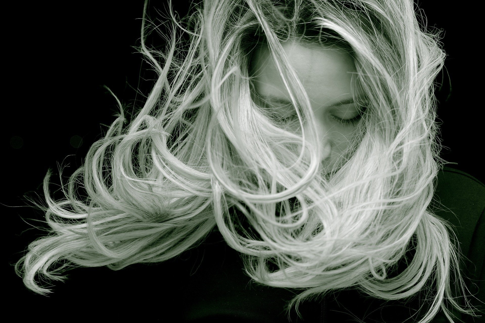 Foto preta e branca de mulher com cabelos ao vento e olhando para baixo.