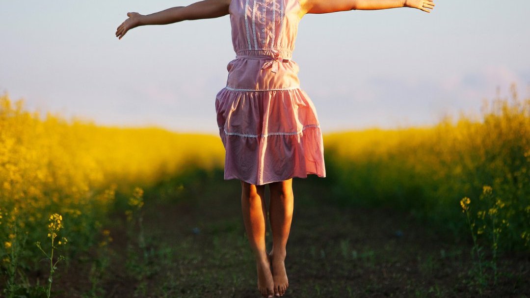 Mulher sorridente pulando de braços abertos em campo de flores