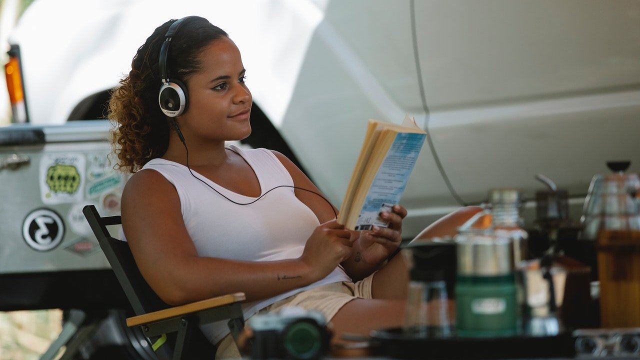 Uma mulher sentada na cadeira com fone de ouvido lendo um livro.