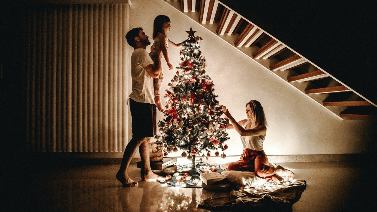 Uma criança com seus pais decorando uma árvore de Natal.