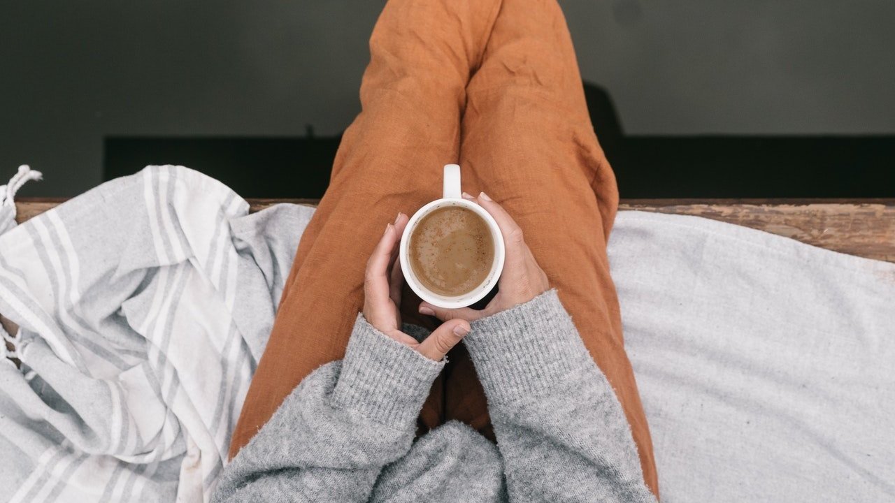 Mulher segura xícara de café sobre as pernas.