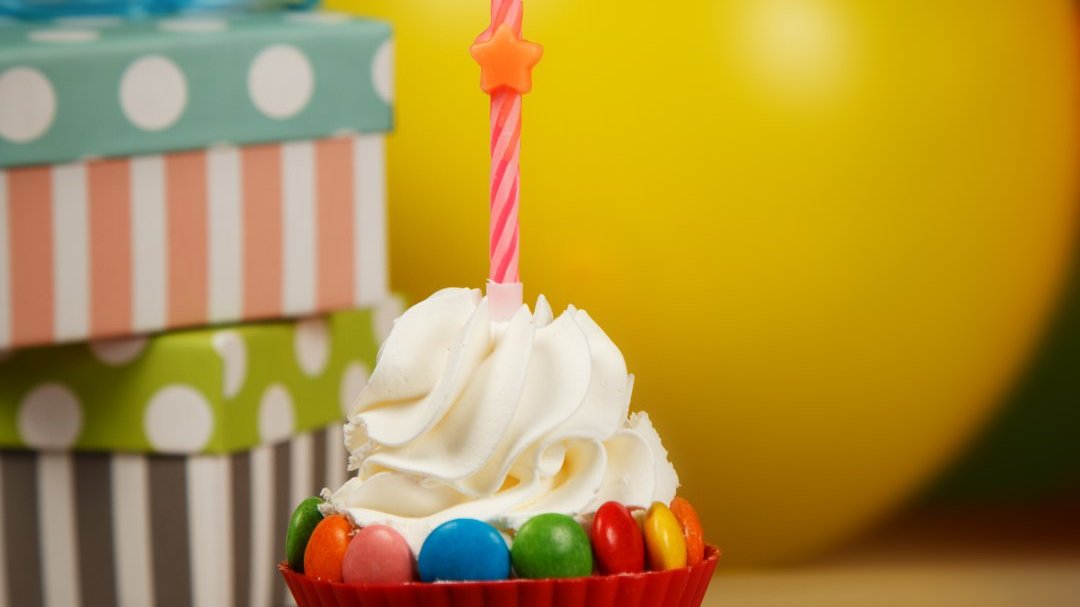 Cupcake com velinha de aniversário ao lado de presentes e balões de festa