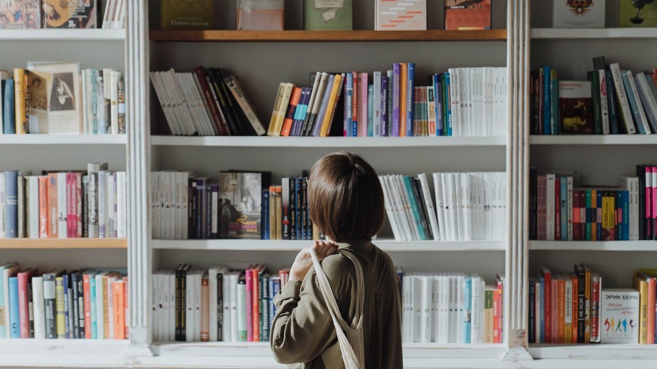 Menina parada em frente a uma instante olhando os vários livros.