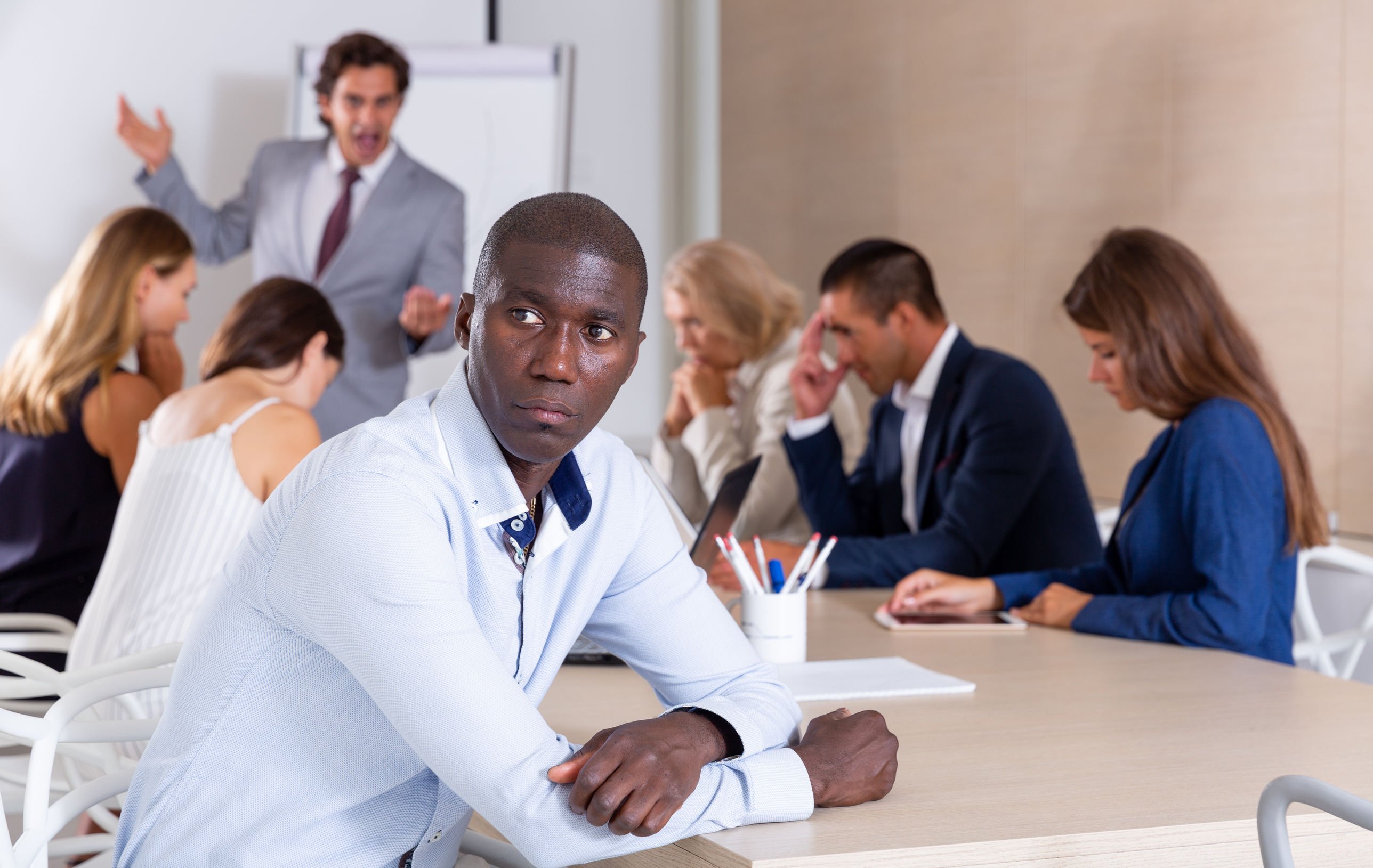 Homem negros, destacado em reunião. Pessoas ao fundo da imagem.