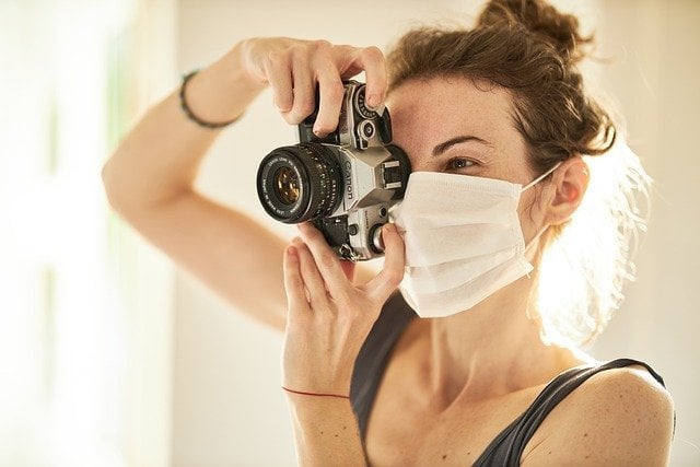 Mulher usando máscara e tirando foto com câmera fotográfica