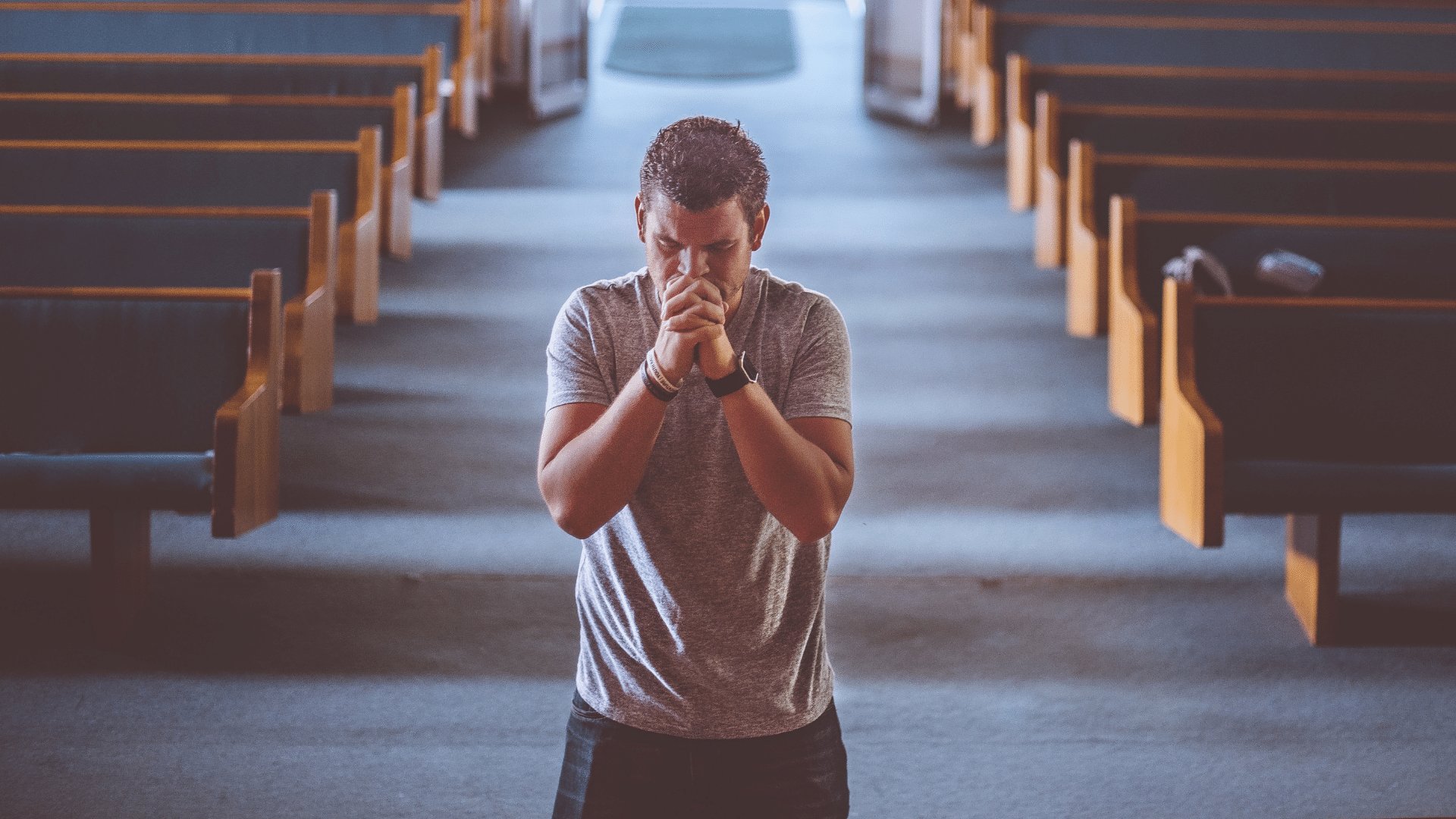 Homem rezando ajoelhado no chão da igreja com as mãos unidas e a cabeça abaixada