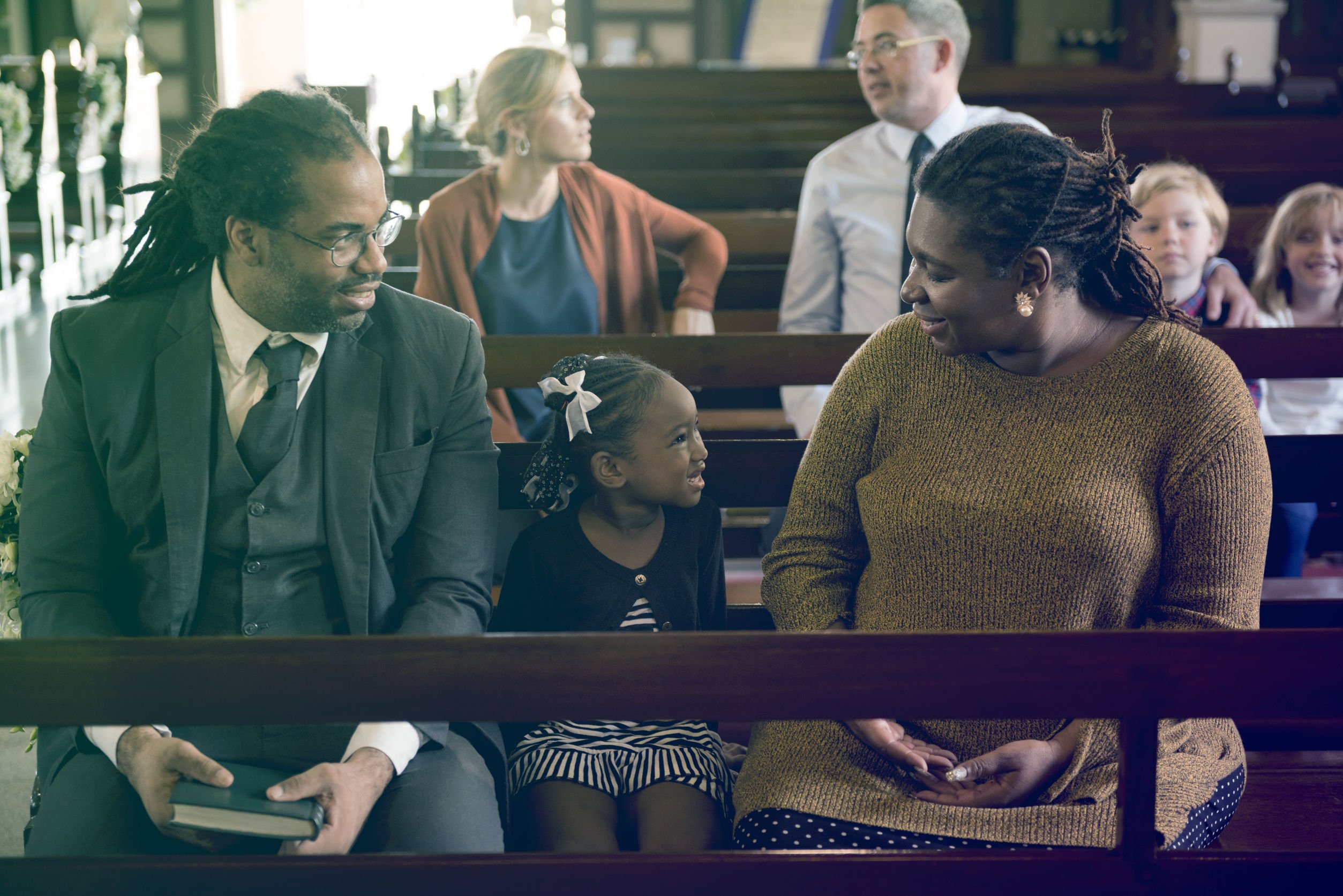Uma família composta de um homem, uma mulher e uma menina sentados juntos em um banco na igreja.