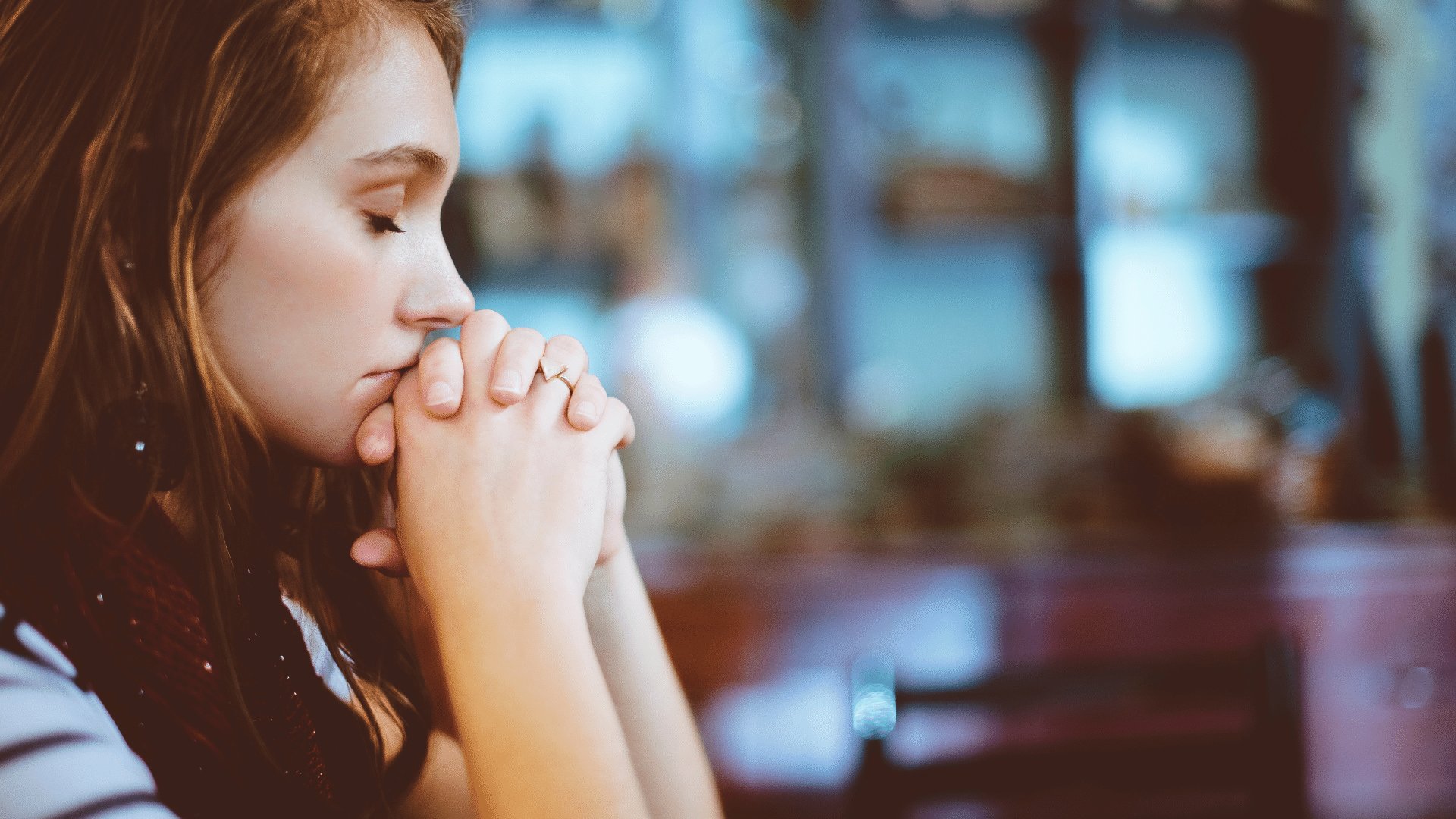 Mulher adulta rezando com os olhos fechados e as mãos unidas