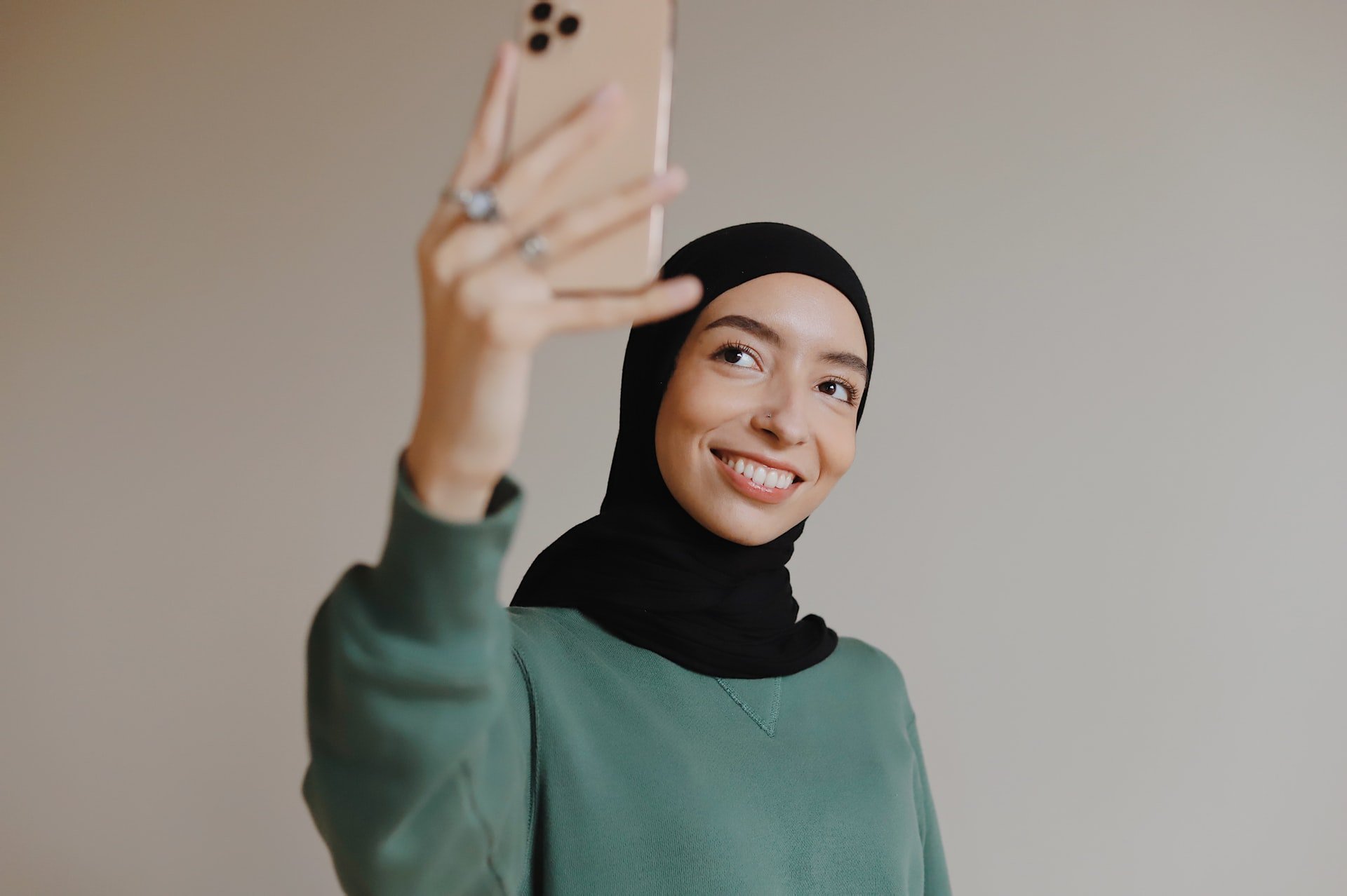 Mulher asiática usando hijab e segurando celular.