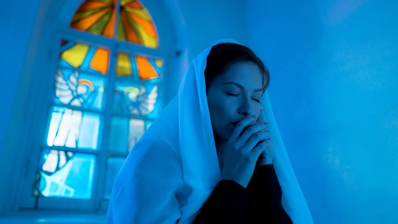 Mulher com véu sobre a cabeça reza em igreja.