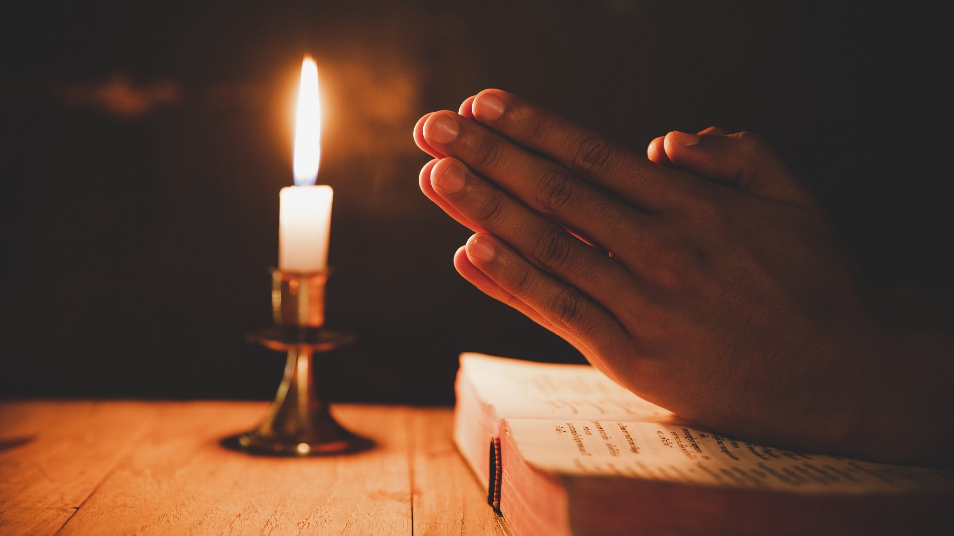 Homem rezando sobre a bíblia com velas acesas
