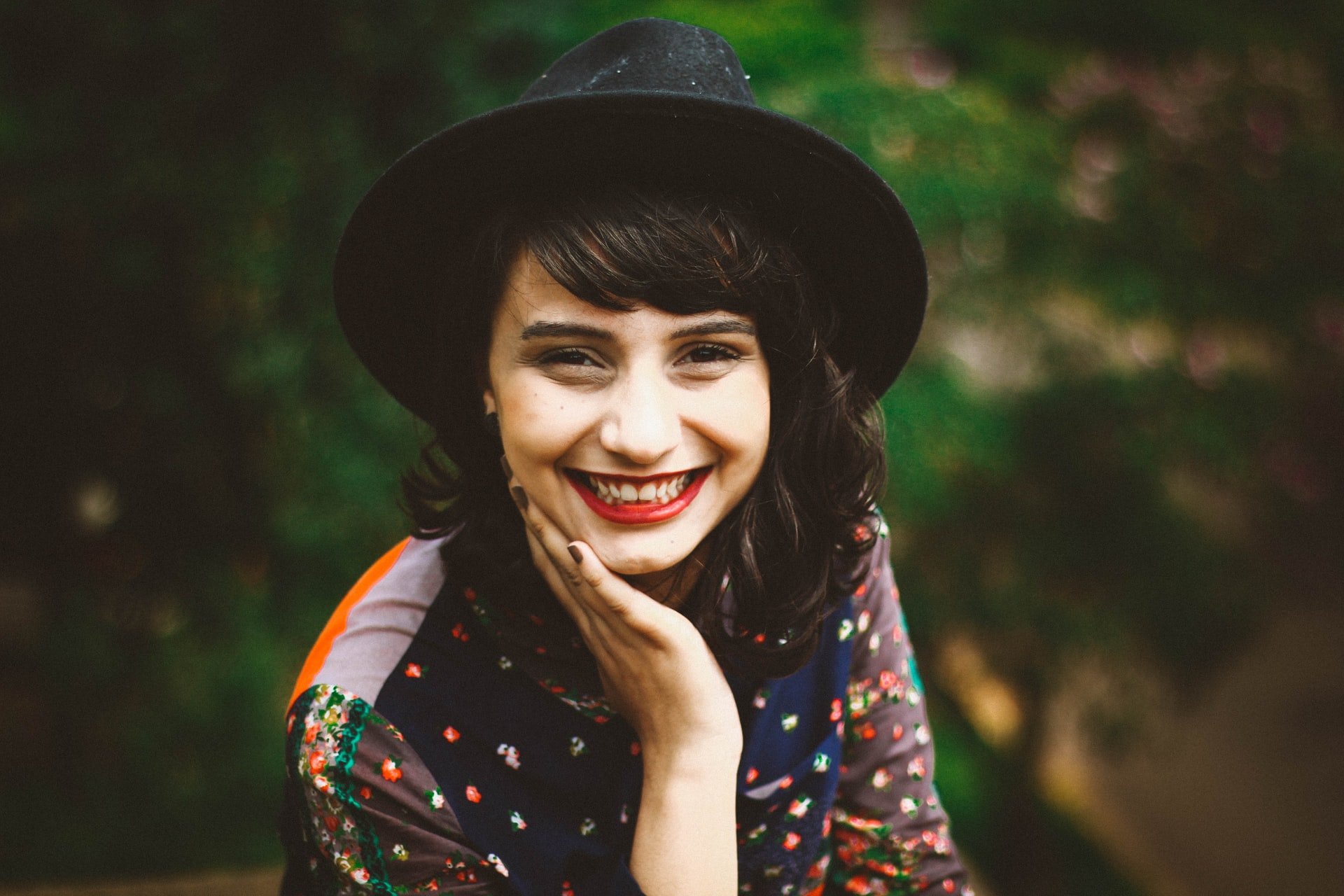 Mulher branca usando chapéu e com a mão no rosto enquanto sorri.