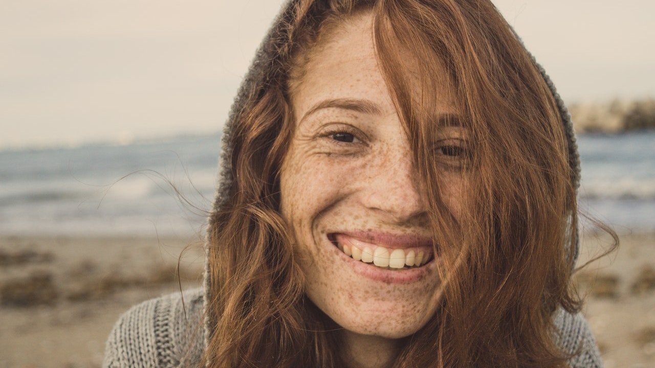Mulher sorri em cenário externo de praia.