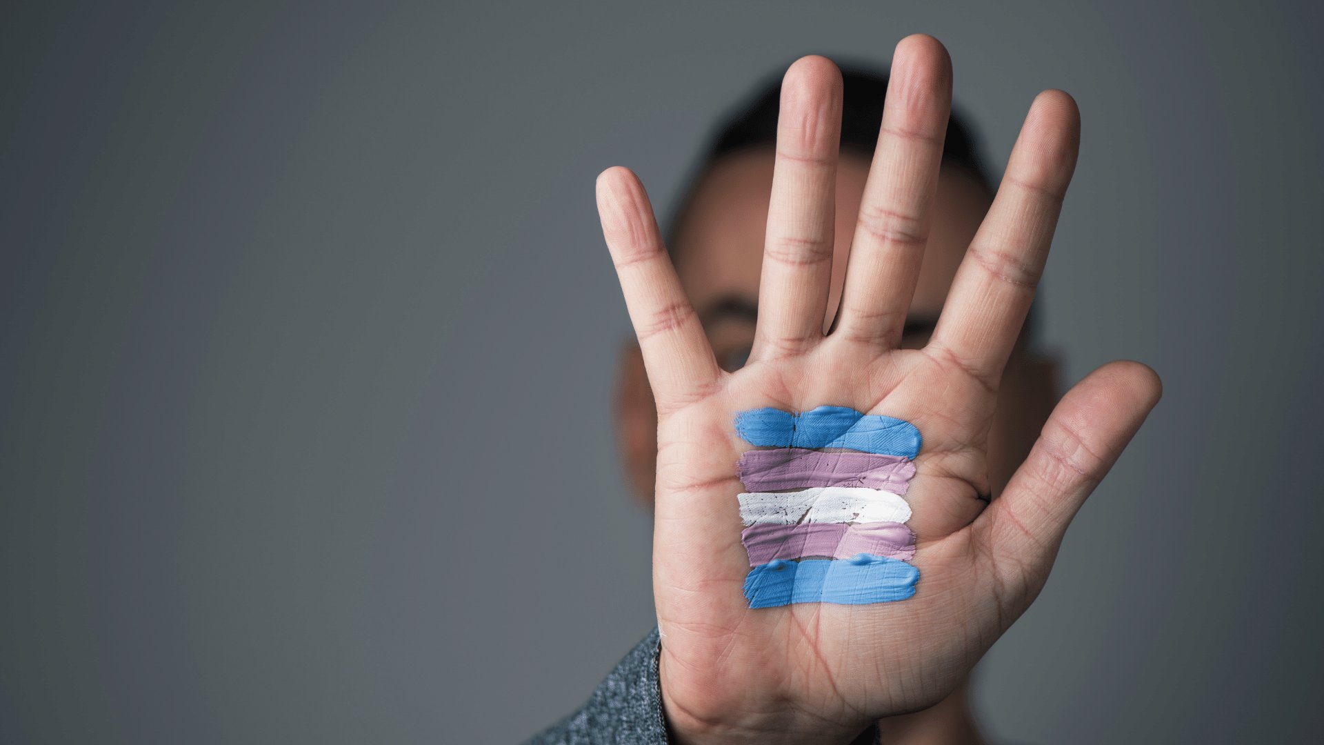Pessoa com uma bandeira trans desenhada em sua palma da mão que está esticada para a câmera