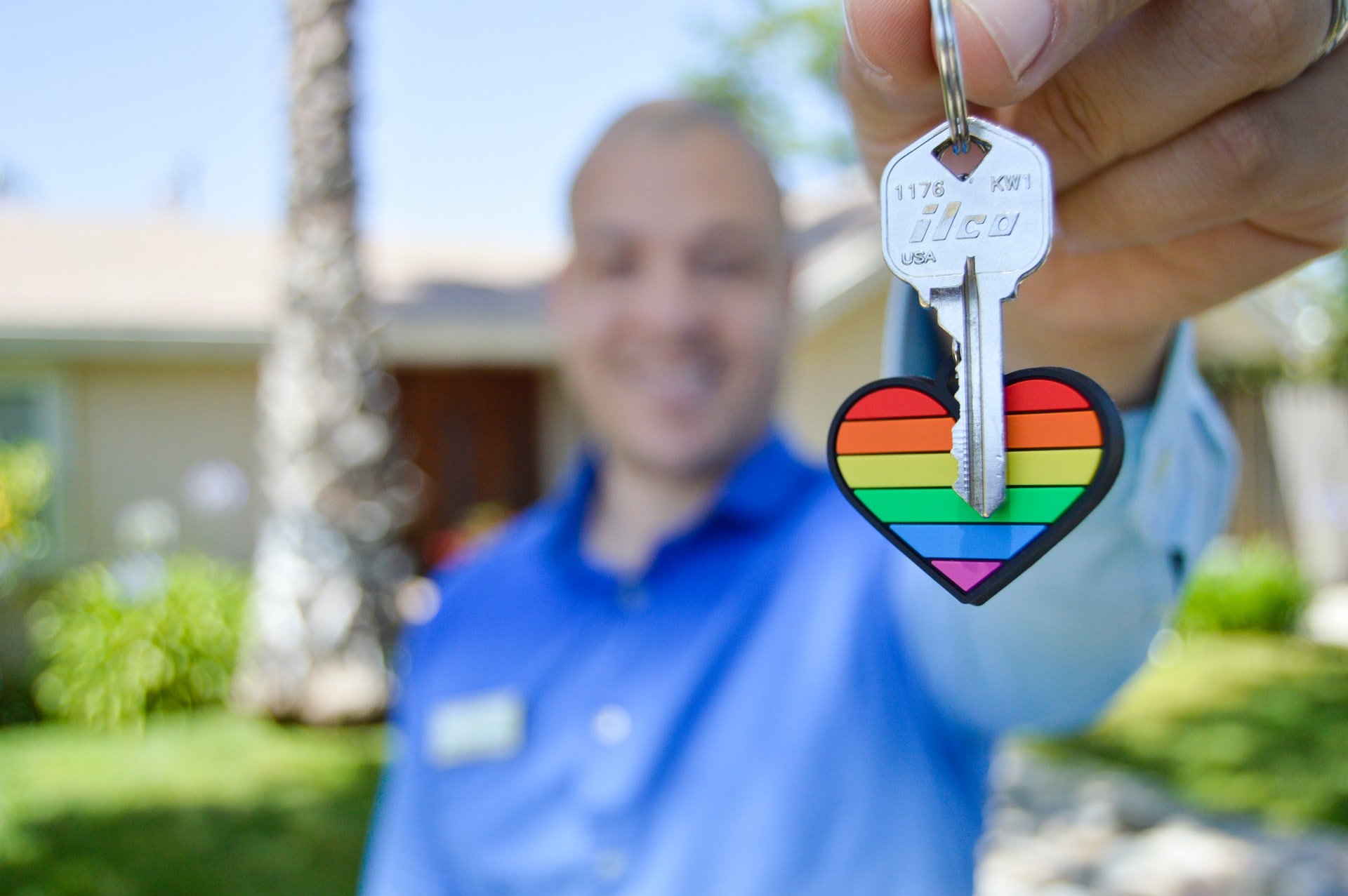 Homem branco segurando chave com chaveiro de coração colorido.