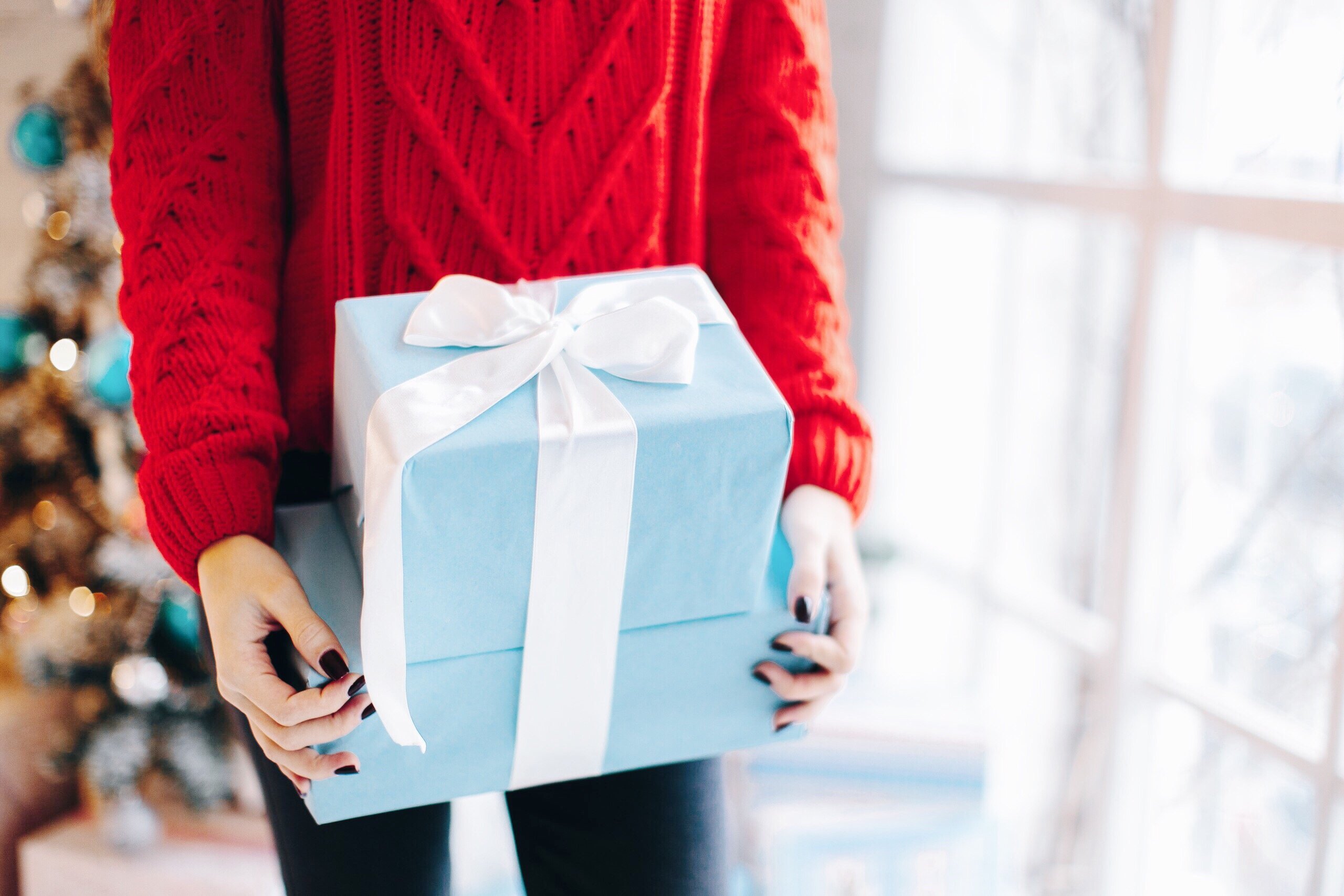 Mulher branca segurando caixa de presente azul.