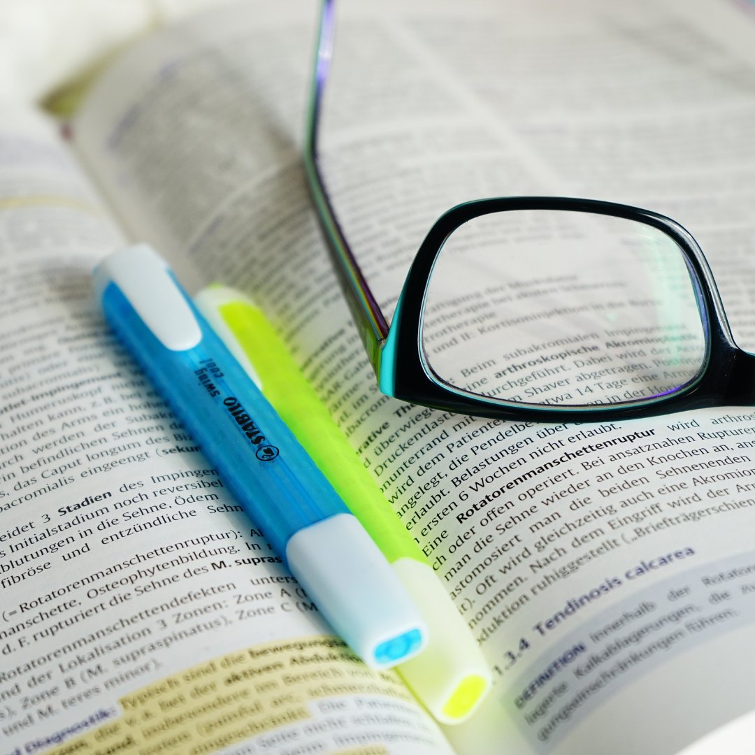 Marcadores de texto e óculos sobre livro.