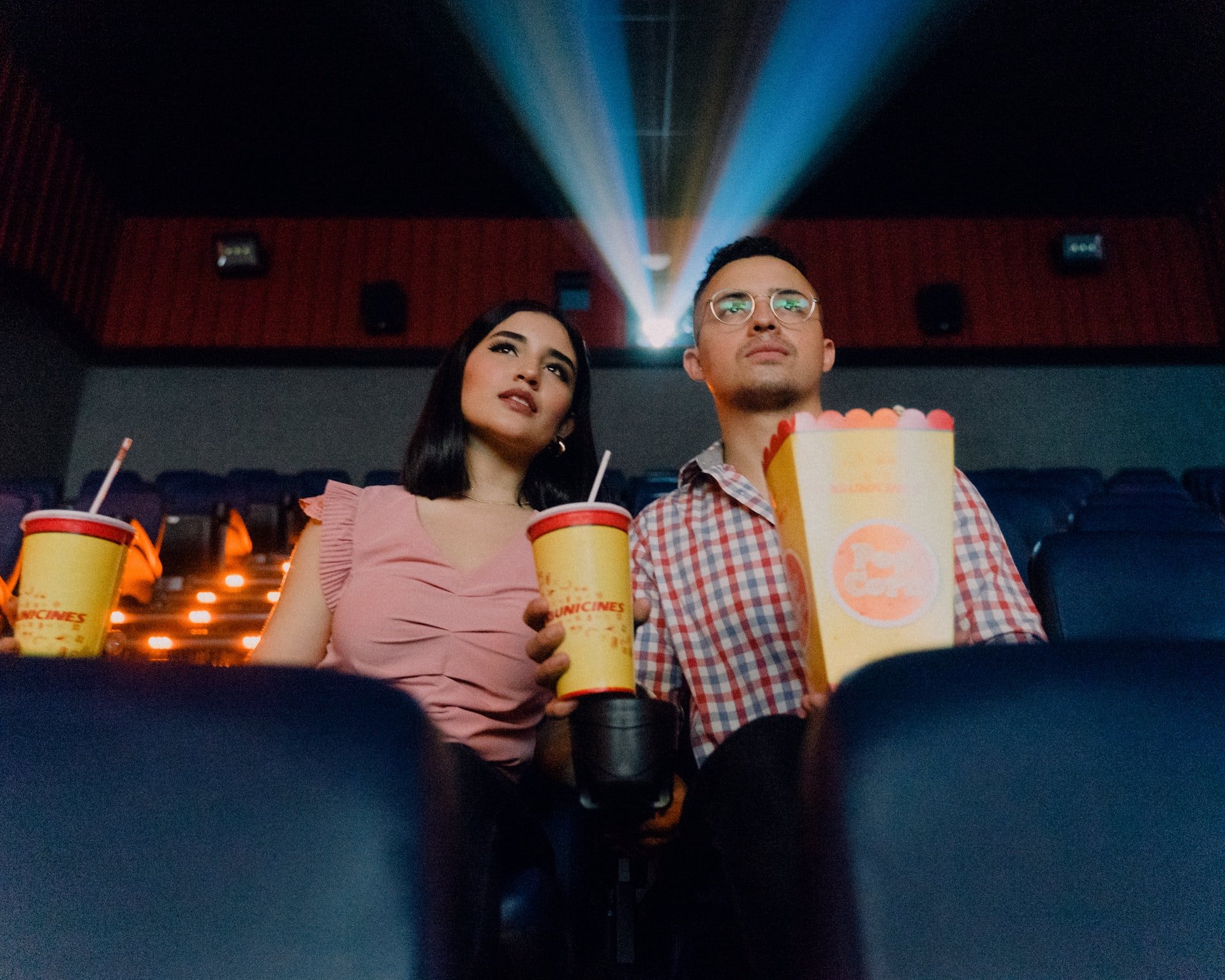 Homem e mulher no cinema segurando pipoca e copo.