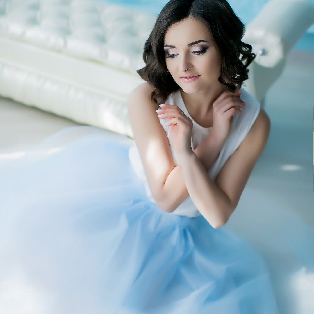 Adolescente sentada apoiada em divã e usando vestido azul