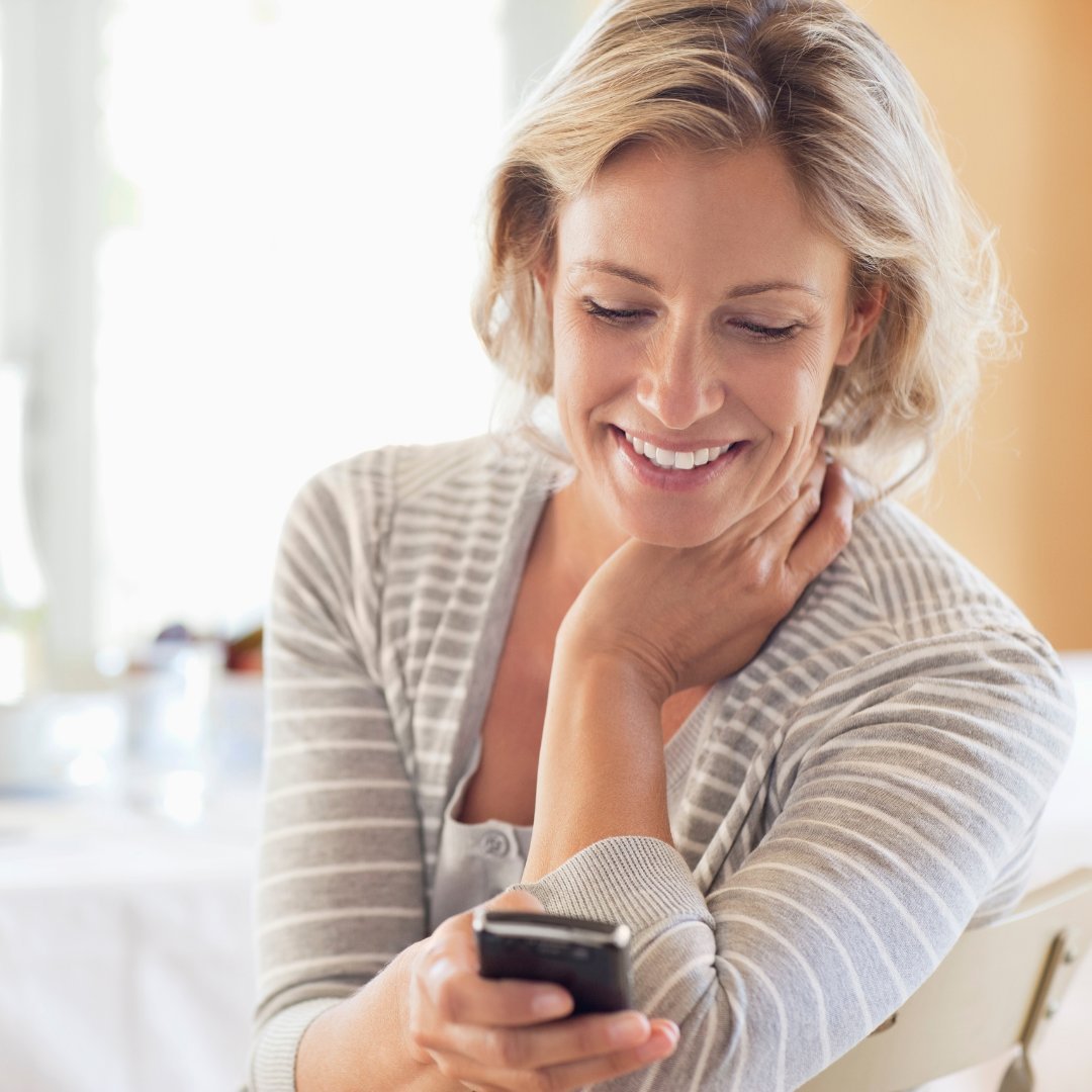Imagem de uma mulher olhando para o celular e sorrindo