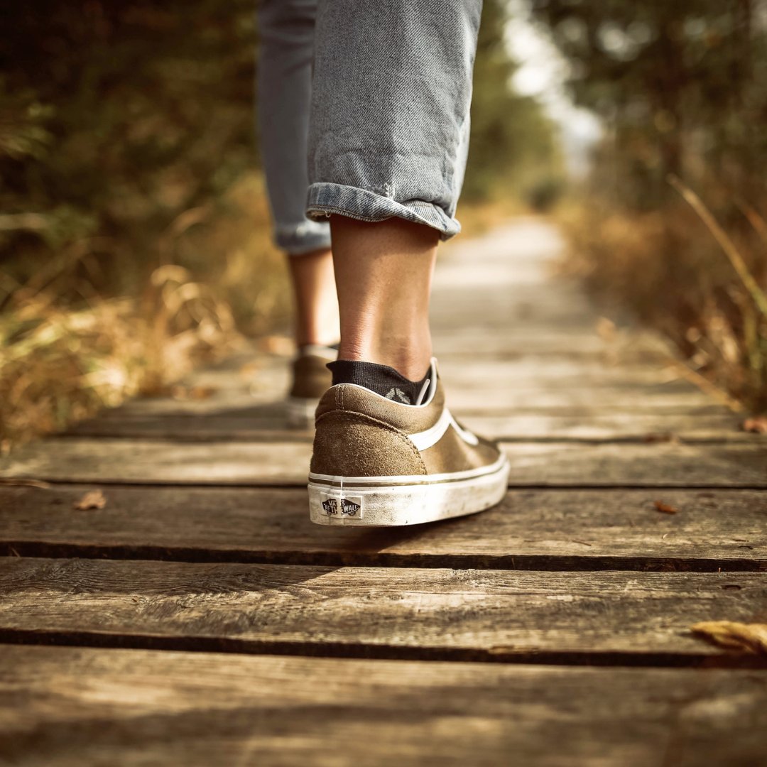 Pés de uma pessoa caminhando no parque sobre caminho de madeira