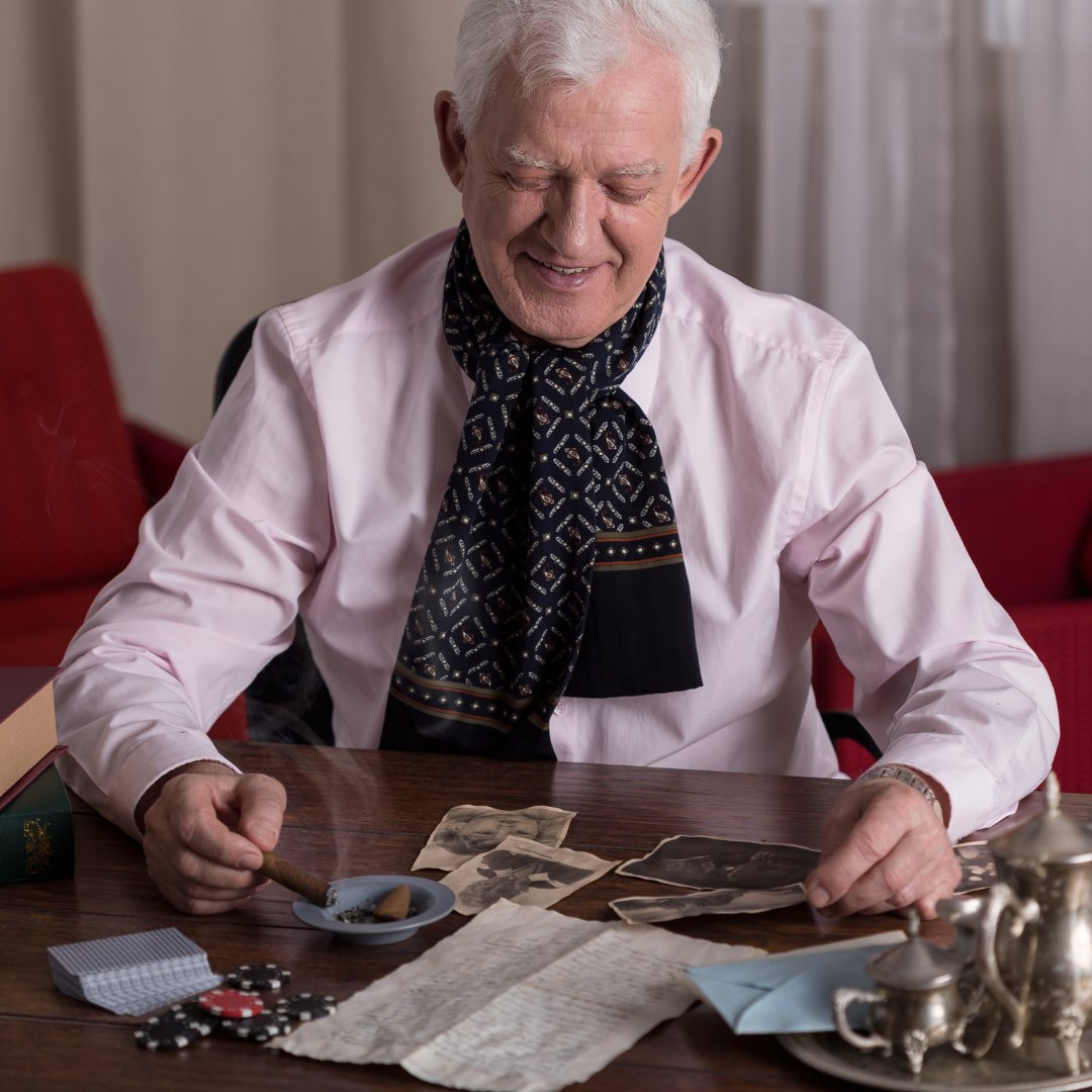 Homem velho sentado olhando fotografias espalhadas em uma mesa