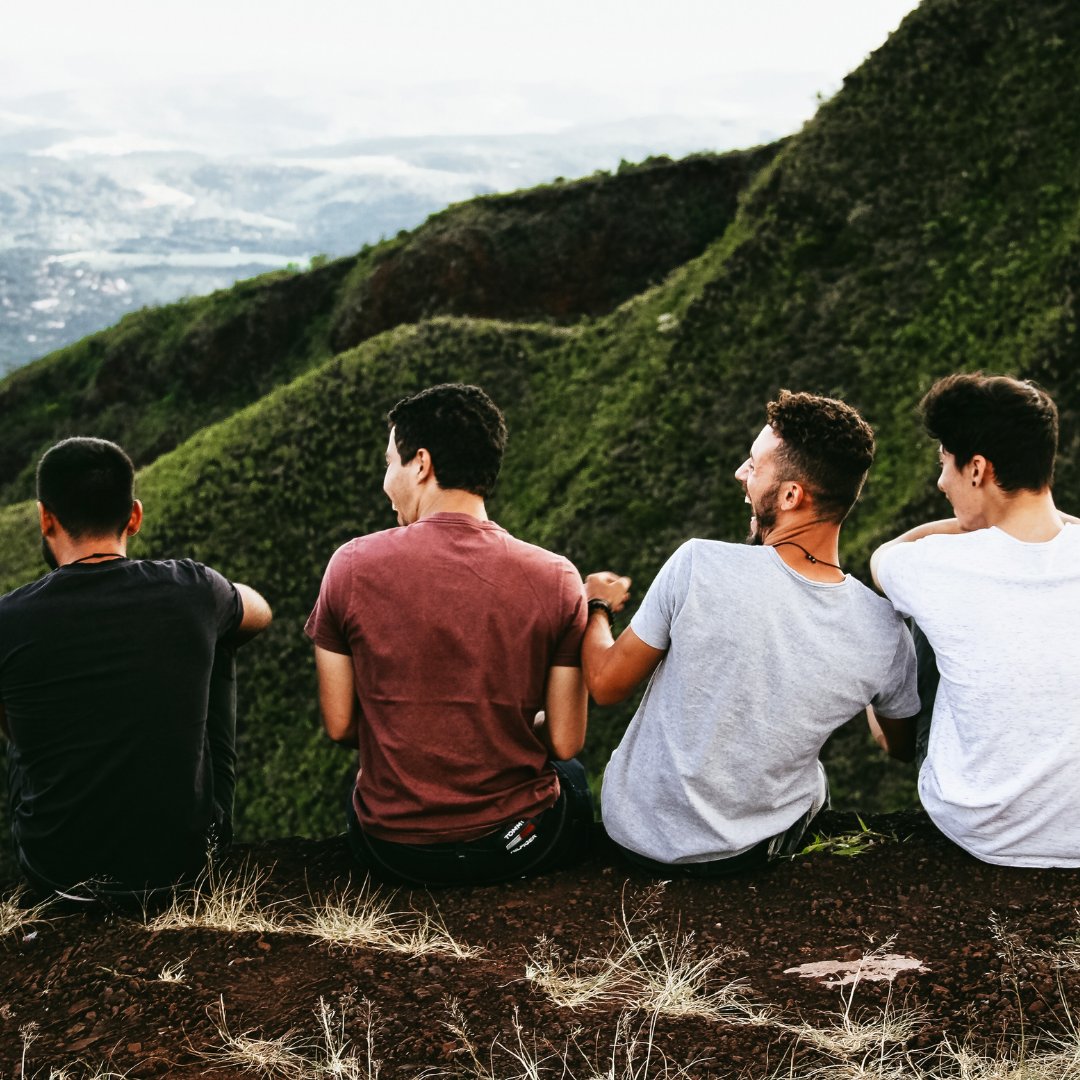 StockSnap / Pixabay / Canva Amigos sentados de costa na beira de uma montanha, dando risada