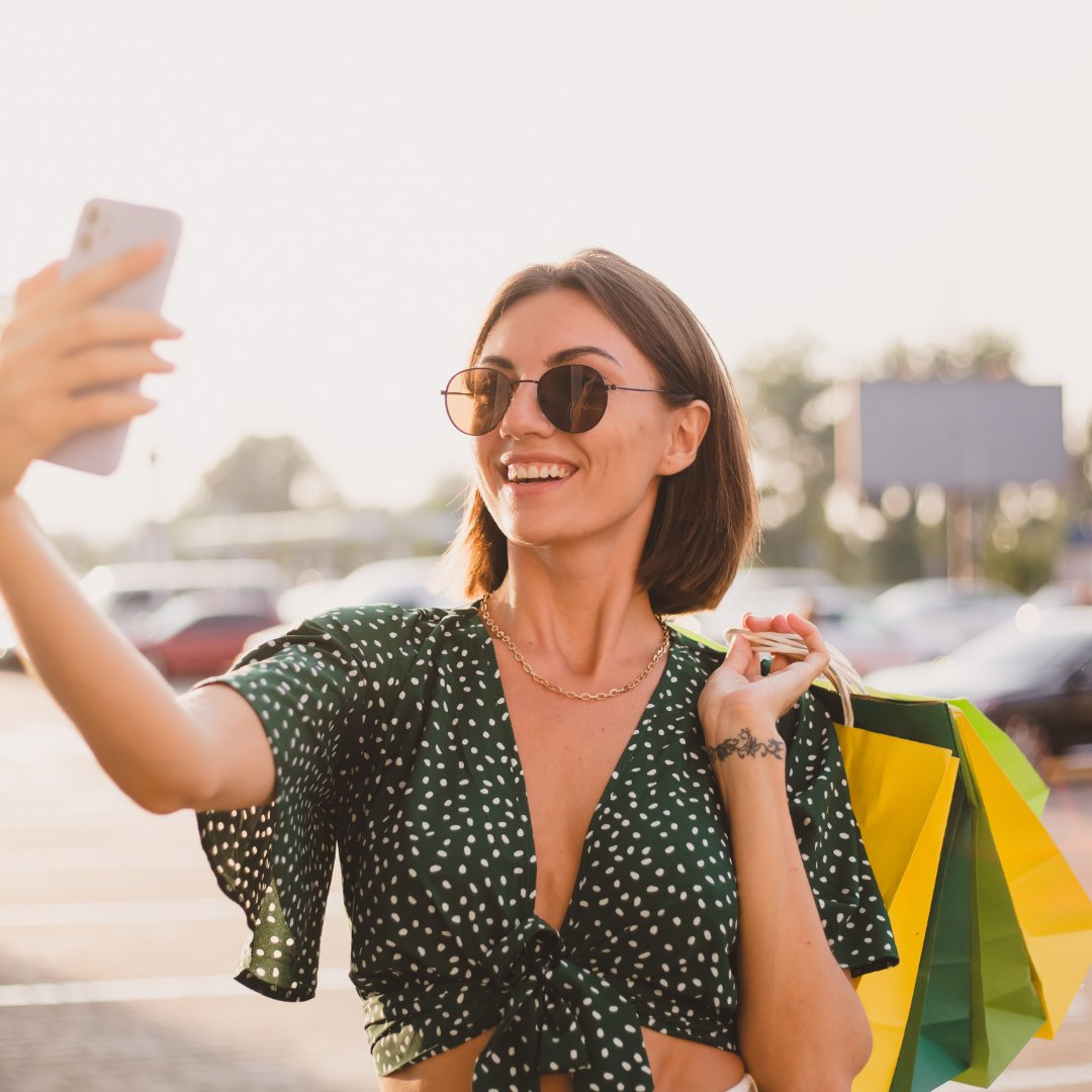 Uma mulher de cabelos curtos capturando uma selfie segurando sacolas de compras
