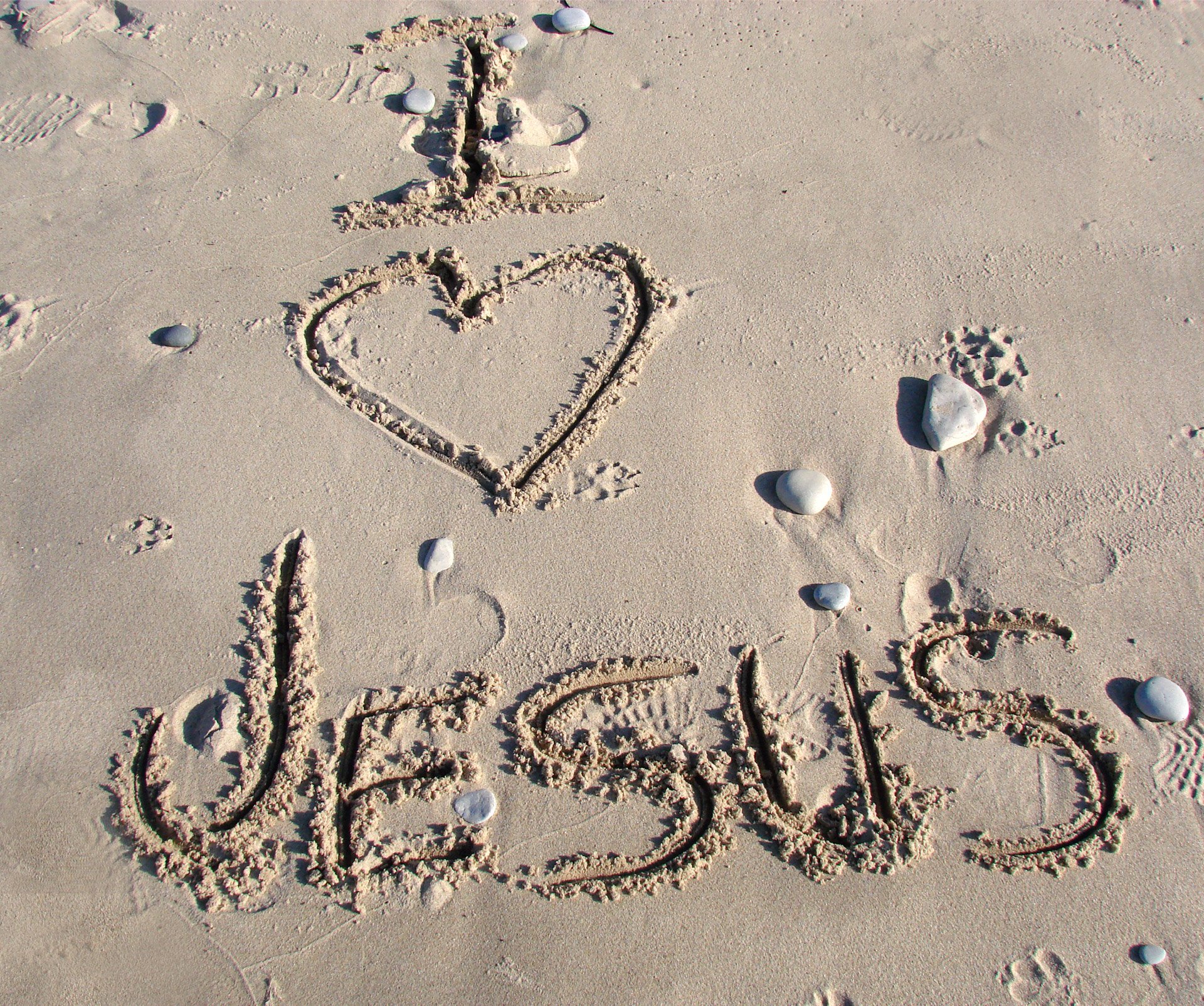 Uma frase grafada na areia: I (coração) Jesus.