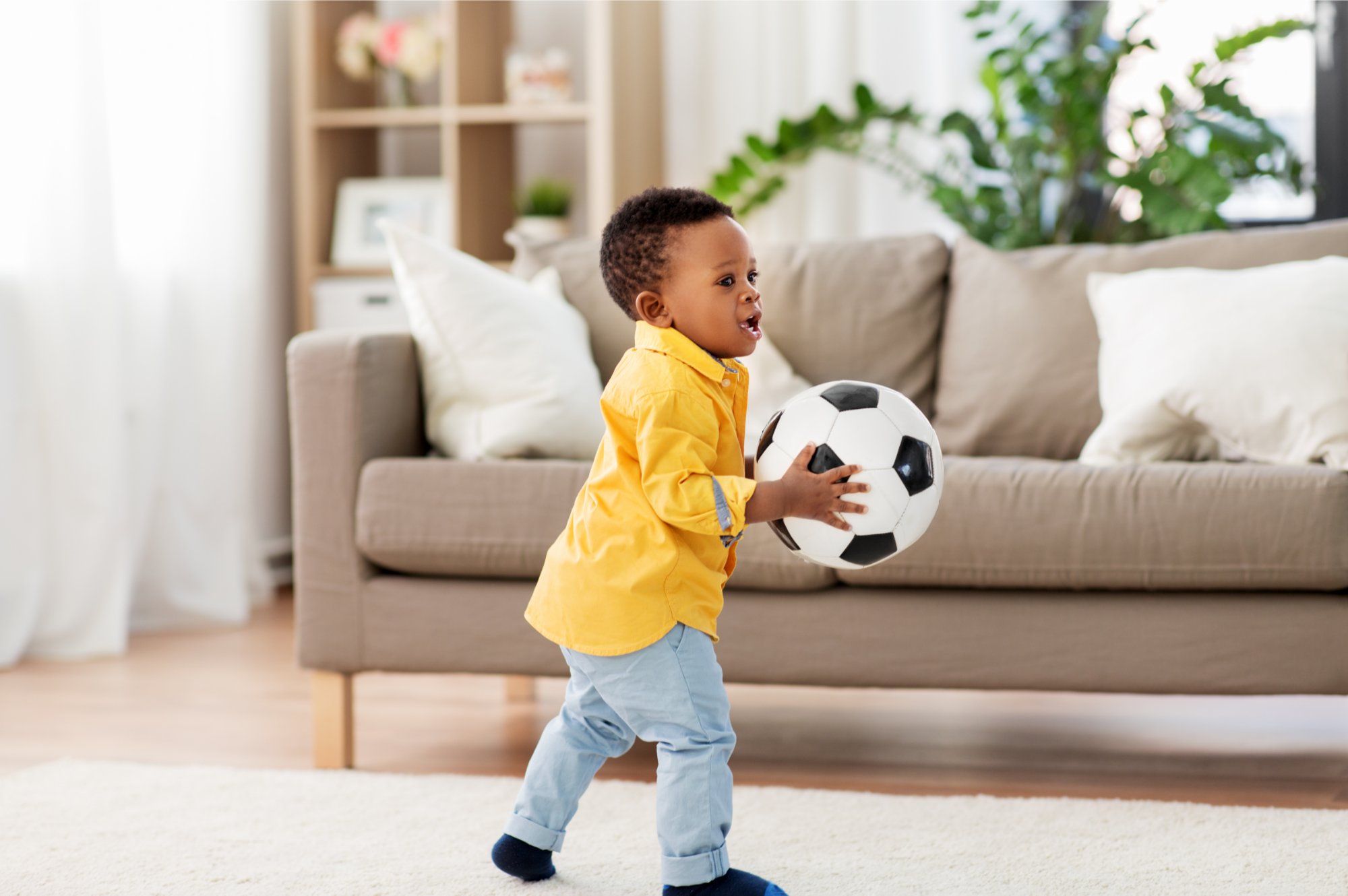 Bebê brincando com bola de futebol numa sala de estar em casa