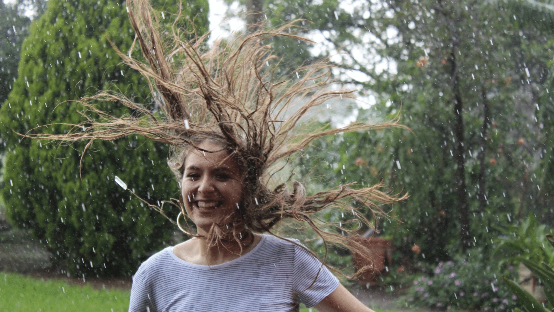 Mulher sorrindo com os cabelos espalhados no ar em meio a natureza