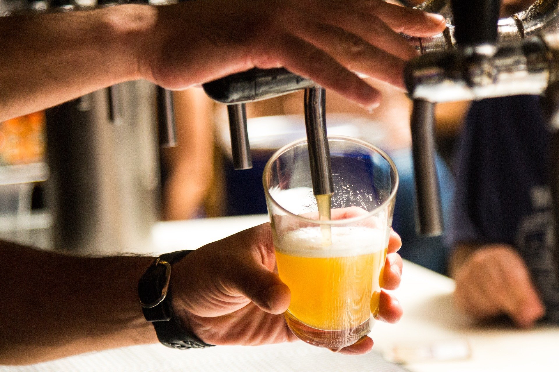 uma mão com relógio de pulso colocando cerveja no copo através de uma torneira