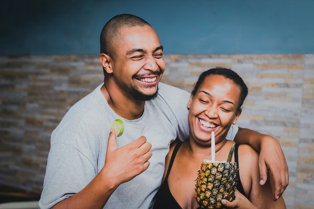 Um homem e uma mulher rindo enquanto ela segura um drink de abacaxi