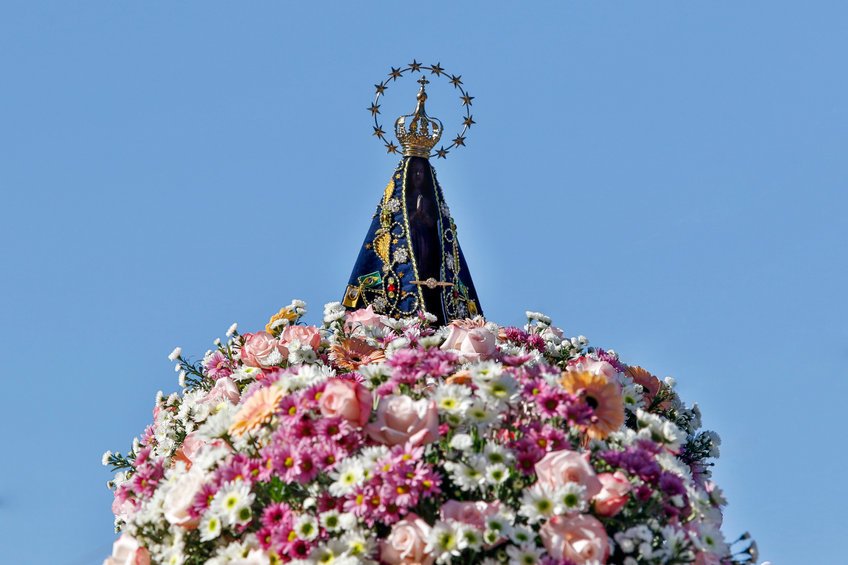Imagem de Nossa Senhora Aparecida sobre um arranjo de flores durante o dia