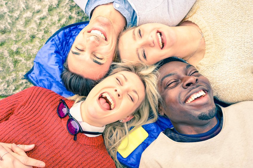 Grupo de amigos composto de duas mulheres e dois homens deitados na grama sorrindo